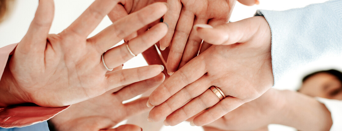 Mehrere Hände, die übereinandergelegt werden, symbolisieren Teamwork und Zusammenhalt.