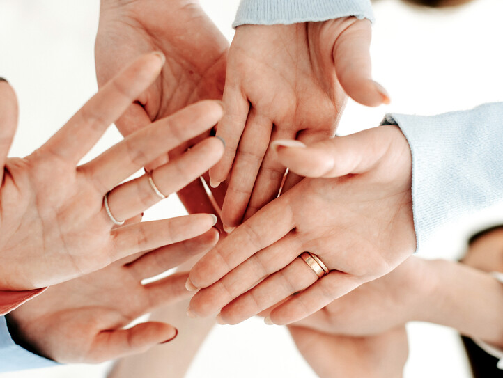 Mehrere Hände, die übereinandergelegt werden, symbolisieren Teamwork und Zusammenhalt.