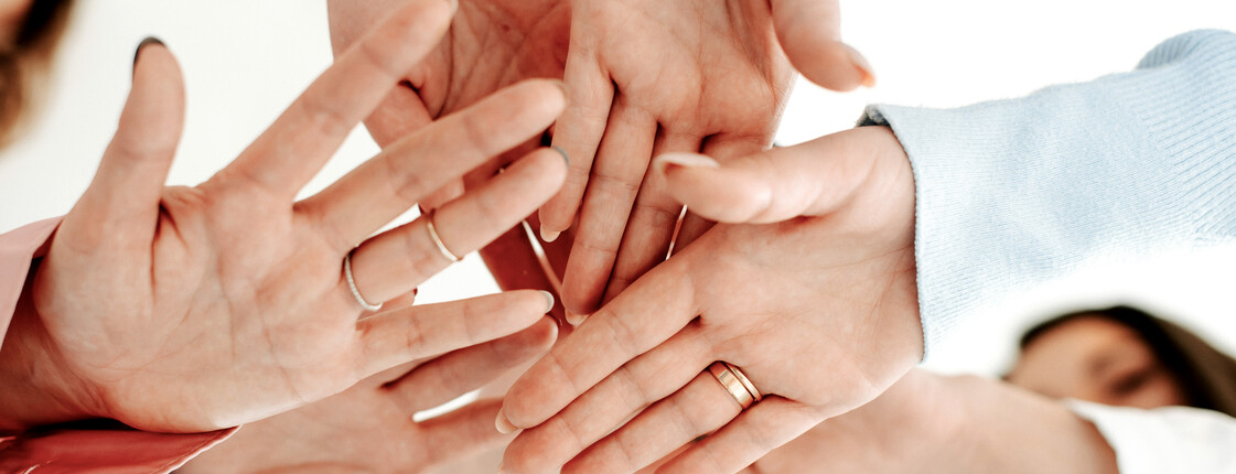 Mehrere Hände, die übereinandergelegt werden, symbolisieren Teamwork und Zusammenhalt.