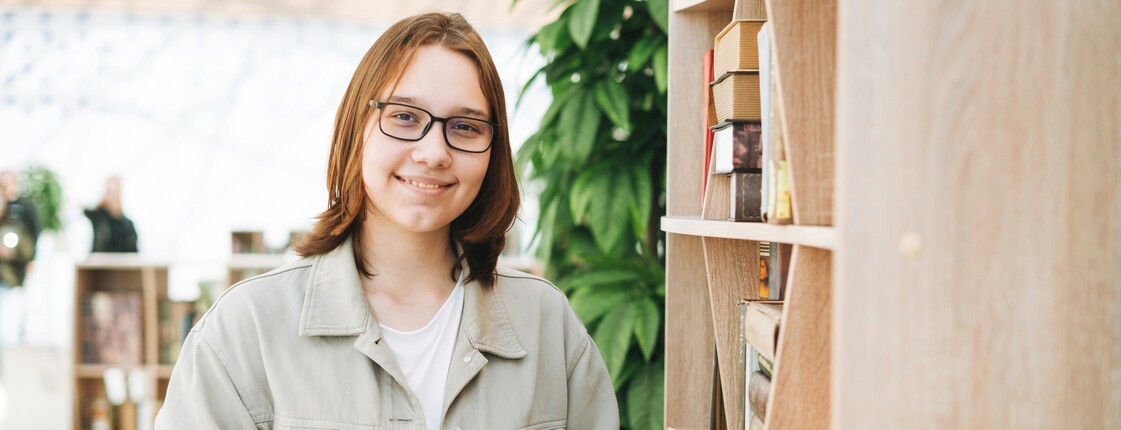 Lächelnde Frau neben Bücherregal mit Handy.